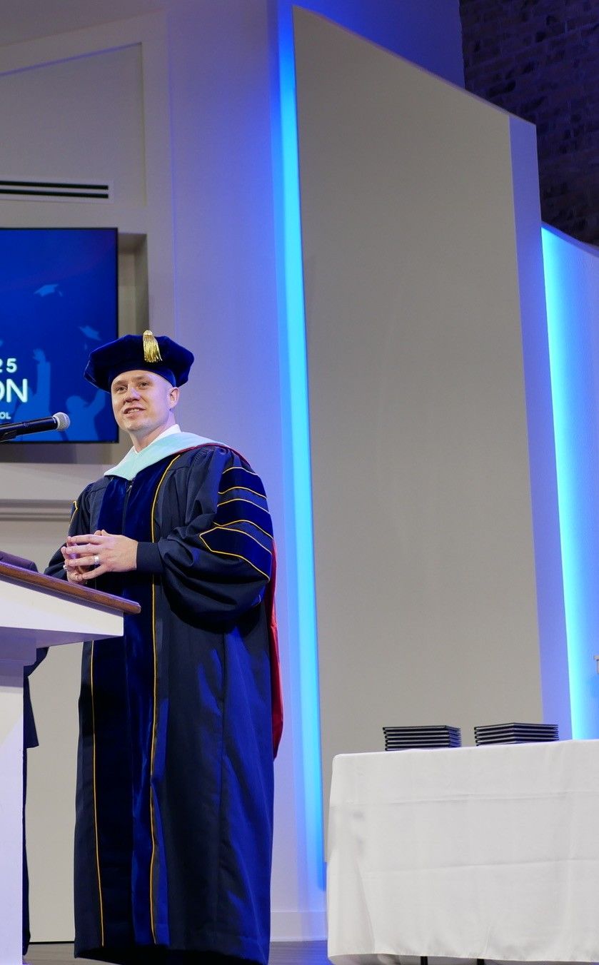 Aaron Glover in doctoral regalia at the podium, addressing King’s Academy Christian School’s class of 2025 graduation