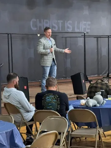 Aaron speaking at a men’s event beneath a “Christ is life” banner