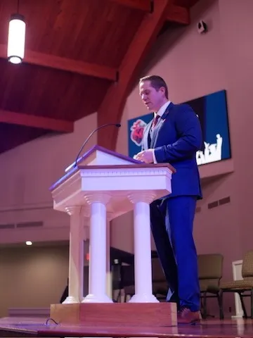 Aaron speaking from a white pulpit at a King’s Academy event