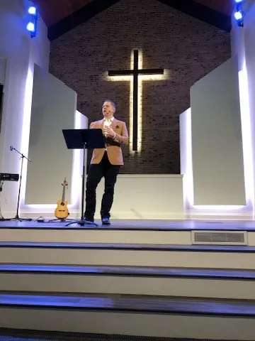 Aaron preaching on a church stage in front of a lit cross