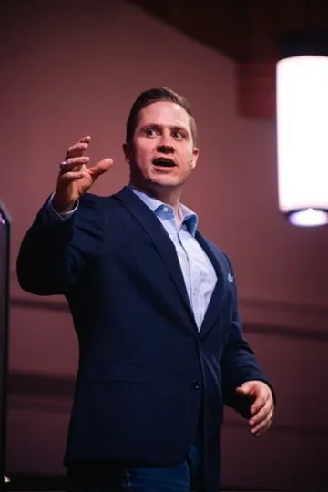 Aaron gesturing mid-message on a dark stage