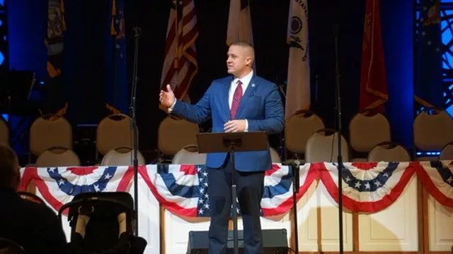 Aaron speaking at a patriotic event in front of flags and bunting
