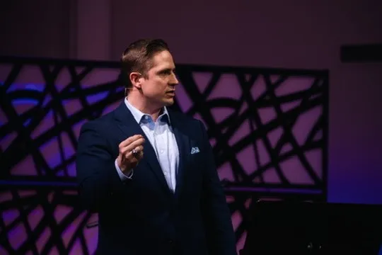Aaron speaking on a purple-lit stage