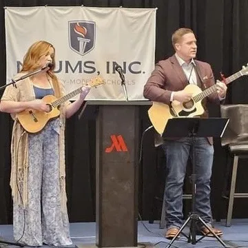Aaron playing guitar and leading worship at a NAUMS gathering of University-Model schools